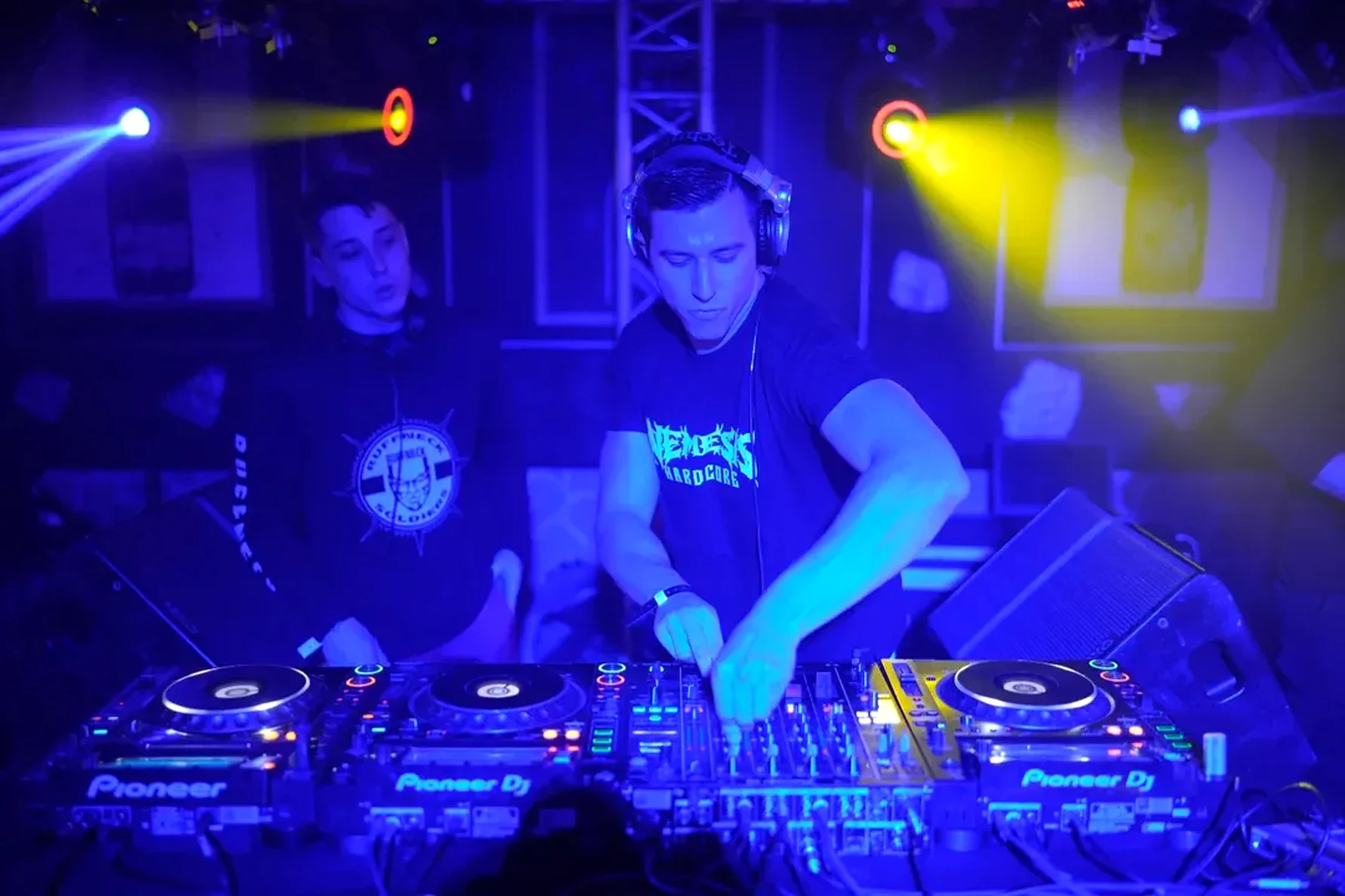 Nemesis Hardcore behind decks under blue light